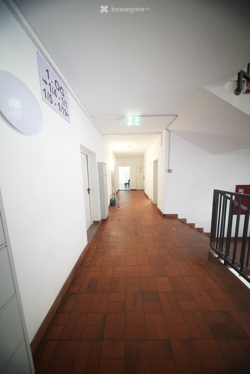Empty hallway with red brick flooring, white walls, and a sign indicating floor numbers.