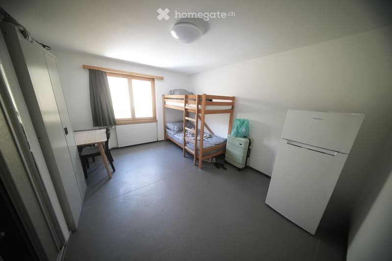 room with bunk bed, table, chair, wardrobe, refrigerator, suitcase, window with curtains