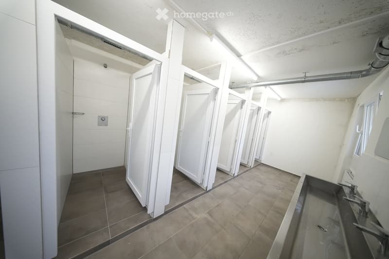 Public restroom with white walls, tiled floor, multiple stalls, and sinks