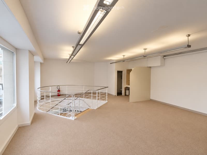 Empty room with beige carpeting, white walls, and a modern white metal staircase leading to an upper level. Features include recessed lighting, a large window, and a small closet area with a door.