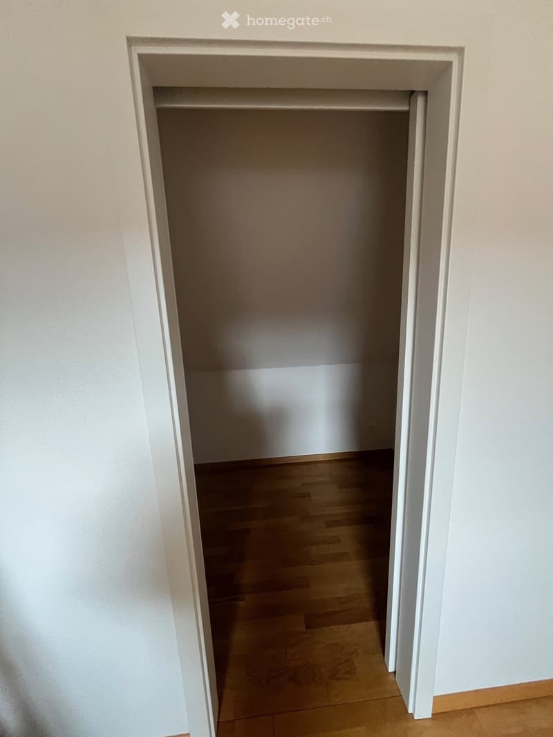 An open closet with wooden floor and white walls.