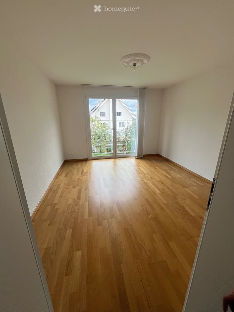 empty room, white walls, wooden floor, sliding glass doors, exterior view of a house and trees