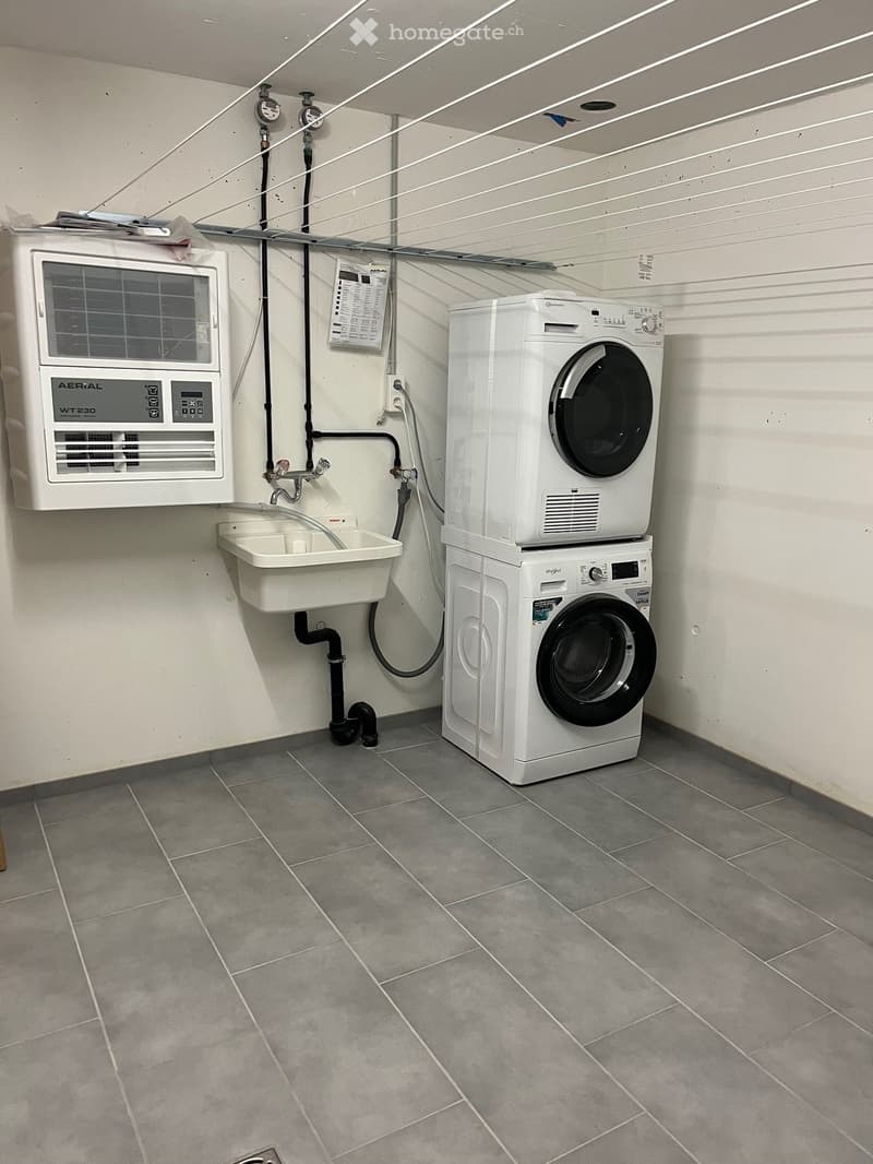 A laundry room with an air conditioner, a sink, and two white washing machines stacked on top of each other