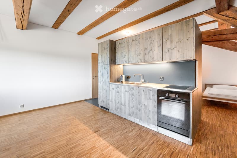 kitchenette with sink, oven, microwave, wooden cabinets, wooden floor, white walls, small sleeping area