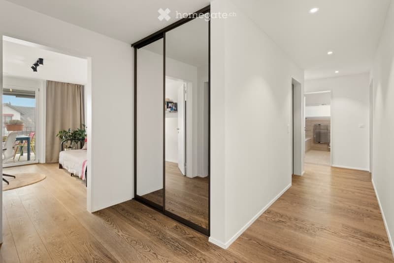 Spacious room with a sliding mirror door, wooden floor, white walls, bed with a single bed, small rug and a bedsheet, a patio with a table and chairs visible from the glass door, and a potted plant.