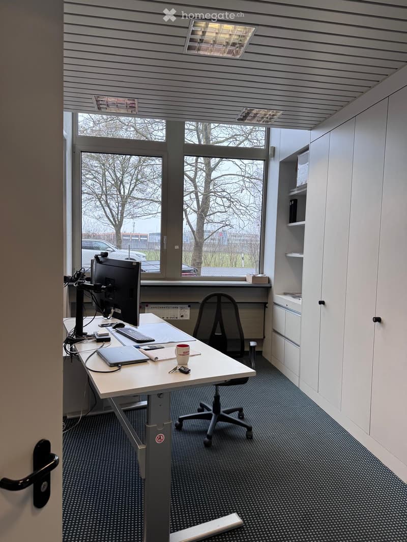 Small office space with a desk, a black office chair, and a computer setup. There is a window providing a view of the outdoors.