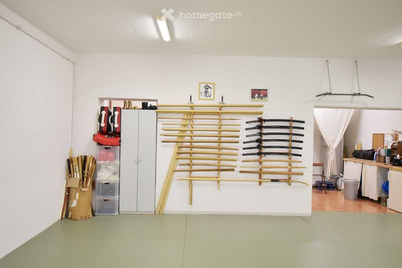empty room, storage boxes, stacks of wooden sticks, sword rack with katanas, white walls, green floor