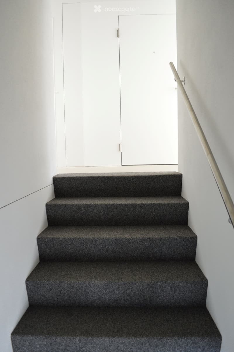 Three steps, grey carpet, white wall, metal handrail