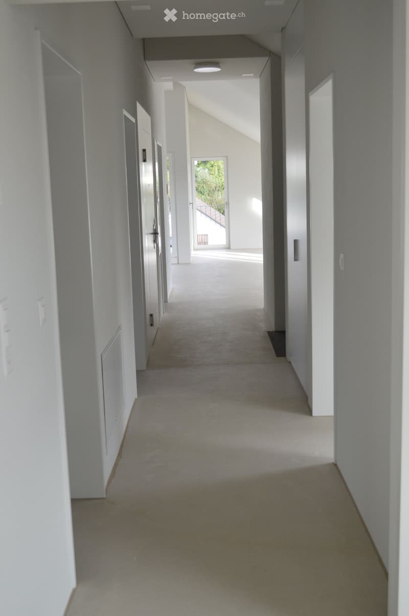 A modern, minimalist corridor with white walls and doors, beige flooring, and ceiling lights