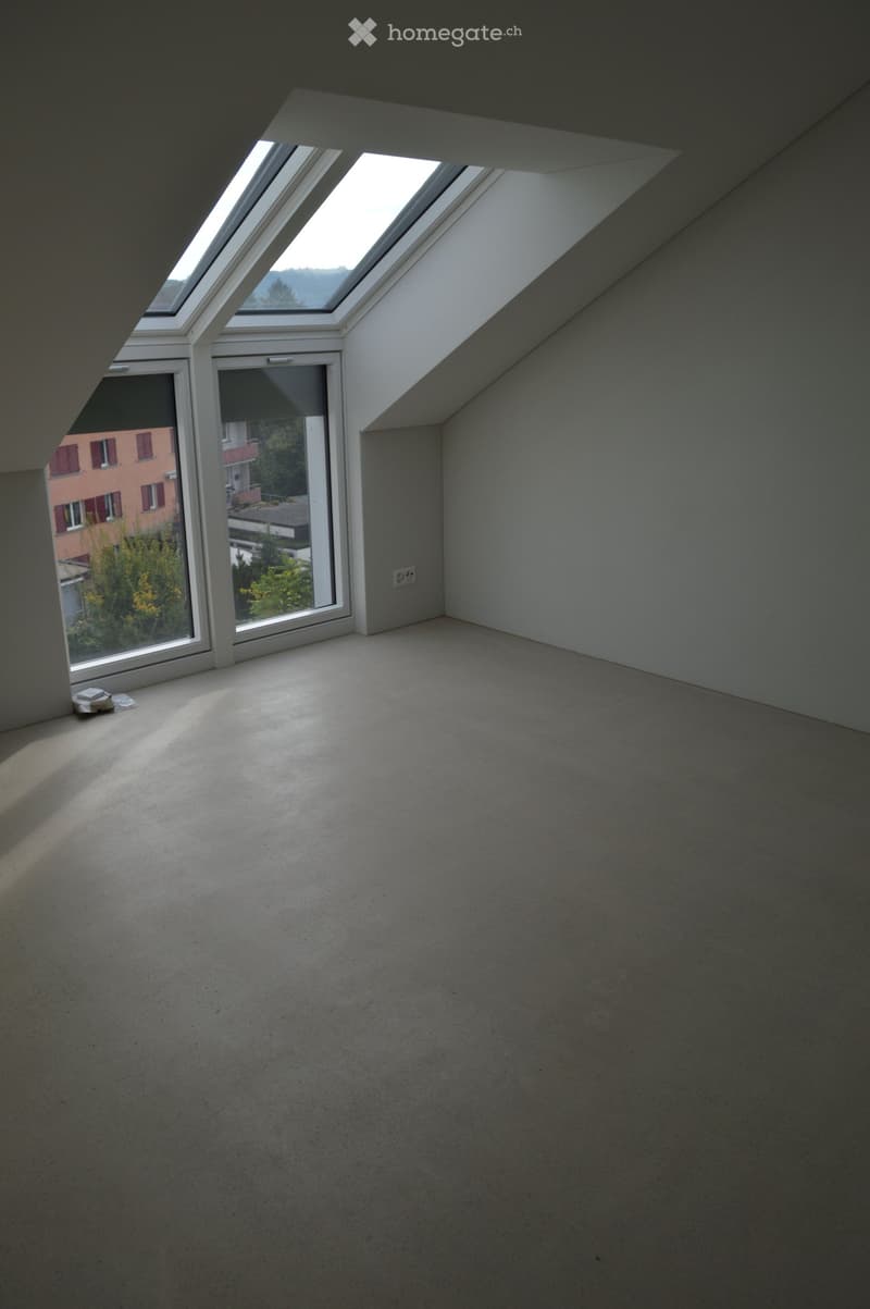 spacious attic room with large skylights, modern white walls, smooth flooring, wall-mounted power outlet