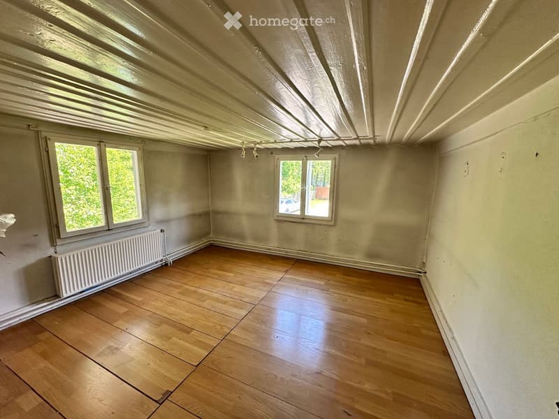 Empty room with wooden floor, white walls, and windows