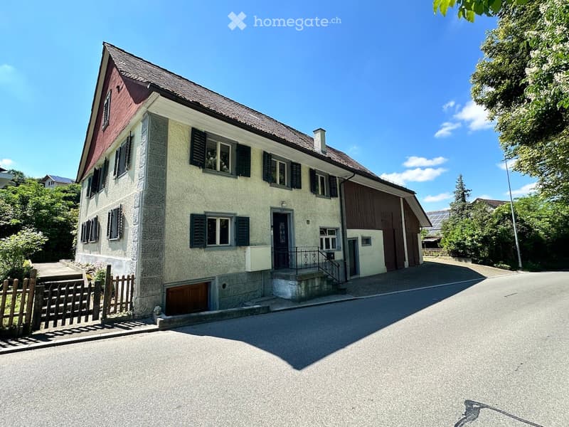 two-story house, red brick, wooden windows, garage, two gates, concrete sidewalk, road, plants, solar panels on roof