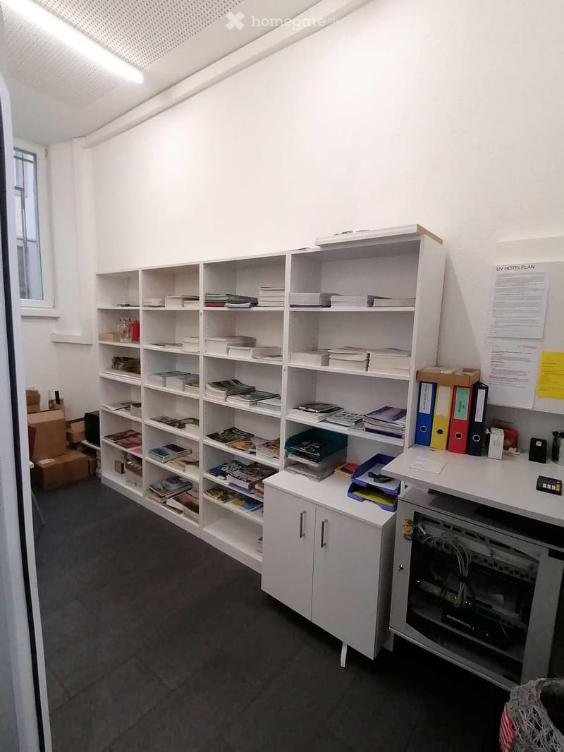 A room with white shelves, filled with books, folders, and a whiteboard with attached papers.