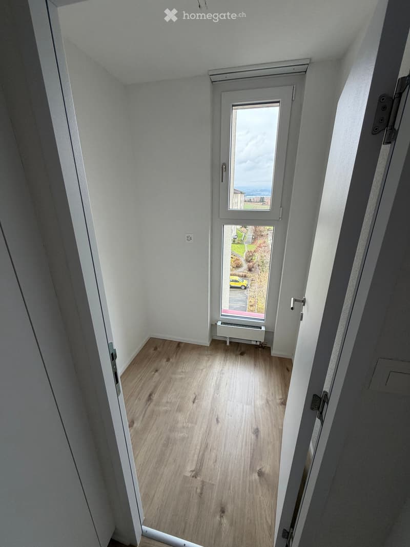 empty room with wooden floor, white walls, window with exterior view, door