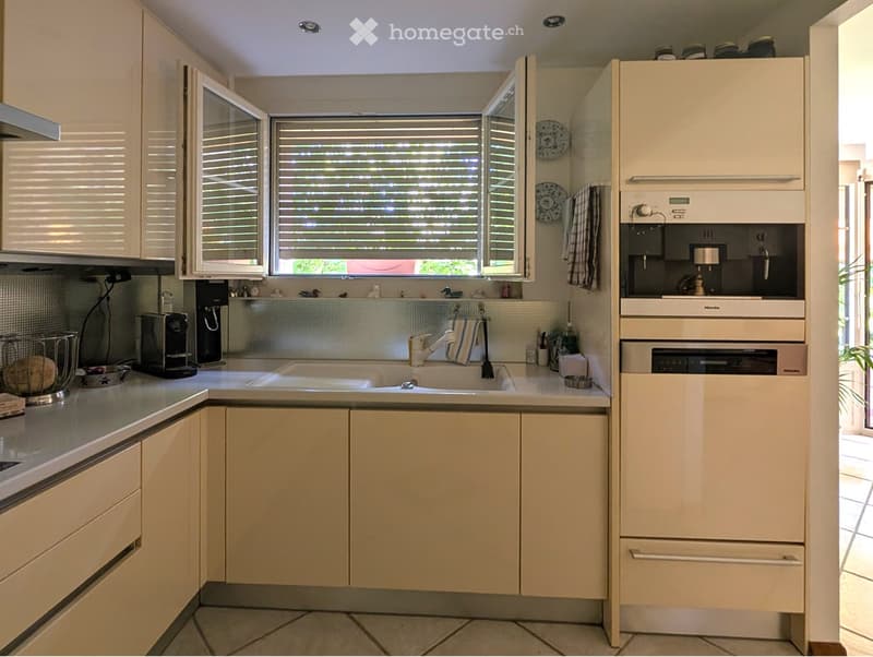 Modern kitchen with a dishwasher, white cabinets, silver appliances, kitchen island, sink, windows, and a coffee machine.