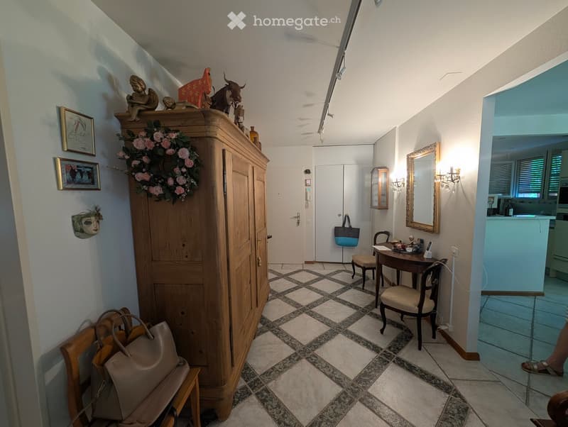 Wooden cabinet, tiles on the floor, paintings on the wall, a desk with a chair, mirror, handbags, a table with a telephone, mirror with wall sconce, bag hanging on the door