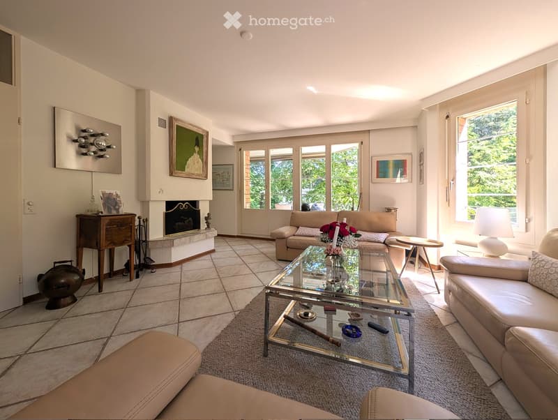 open living room with beige sofa, fireplace, glass table, tile floor, artwork