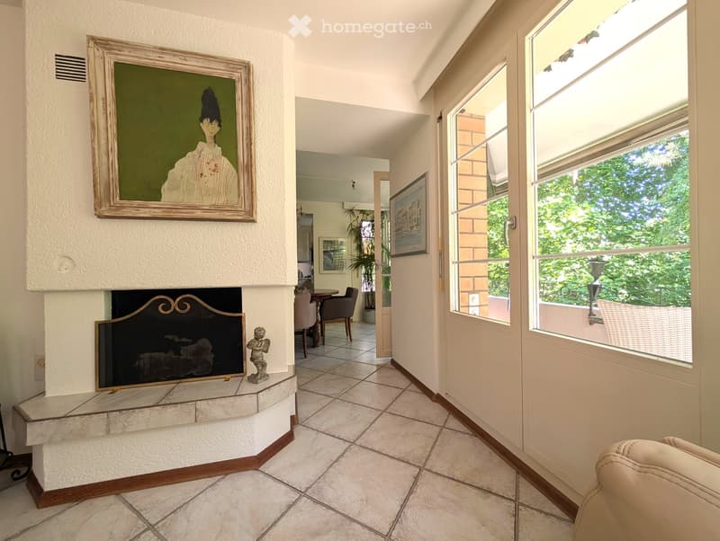 Fireplace, white tiles, large windows, picture frame, tables and chairs, green trees