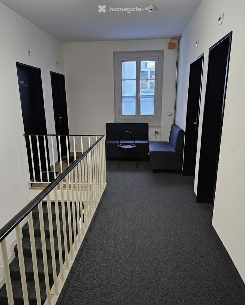 Empty room with carpet, couches and chairs in front of a window, white walls, white stairs with railing