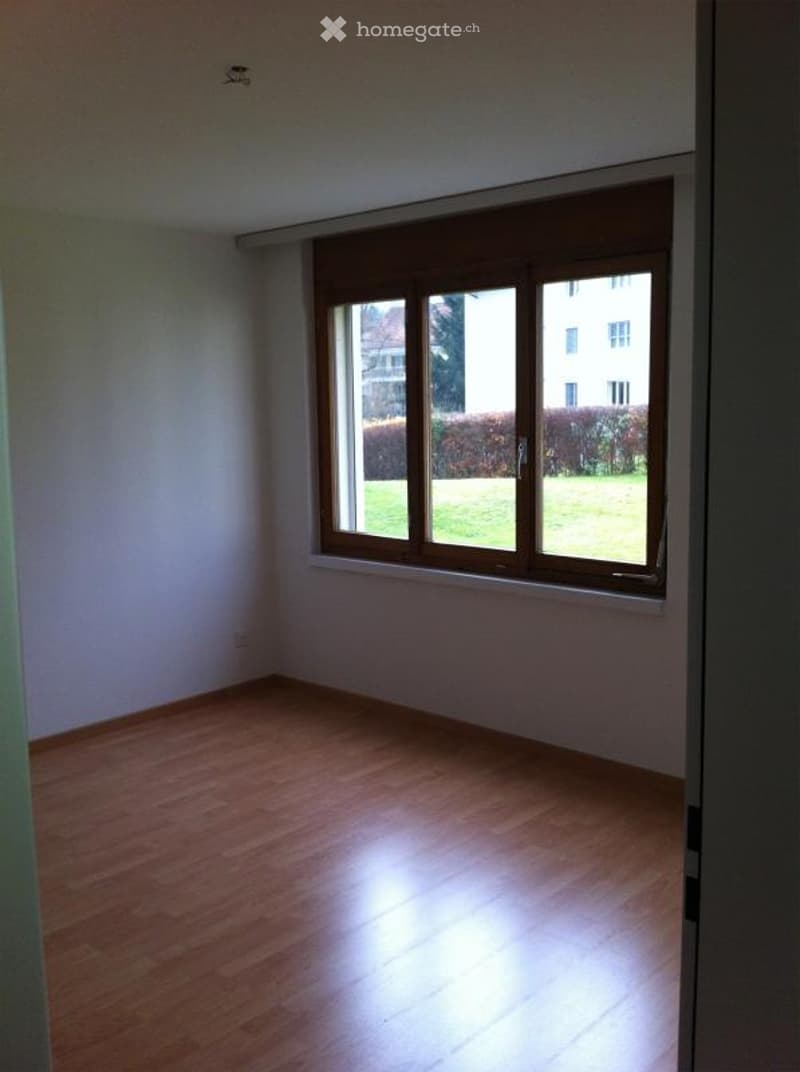 Empty room with wooden floors, white walls, power outlet, window with outside view.