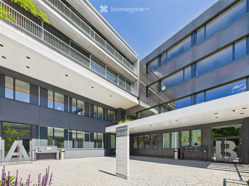 Modern office building with glass walls, multiple floors, and a paved entrance area