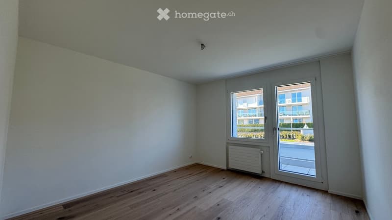 Empty room with white walls, wooden floor, sliding glass door leading to a balcony, heater under the window, no furniture