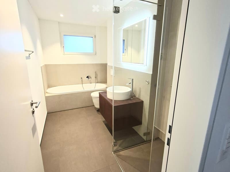 Modern bathroom with glass walk-in shower, white tiles, white sink, bathtub, toilet, vanity cabinet, mirror with lights
