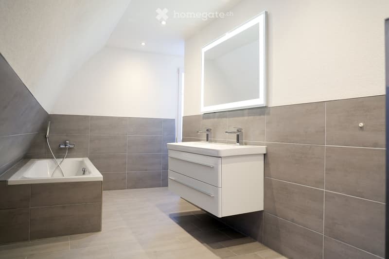 modern bathroom with gray tiles, white bathtub, modern sink, and mirror