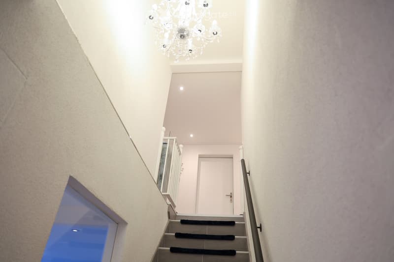 stairs with a black carpet, a white door, a glass window, a white ceiling with a chandelier