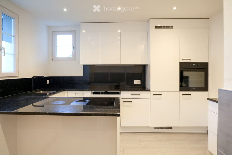 Modern kitchen with granite countertop, white cabinets, modern appliances, and black granite backsplash