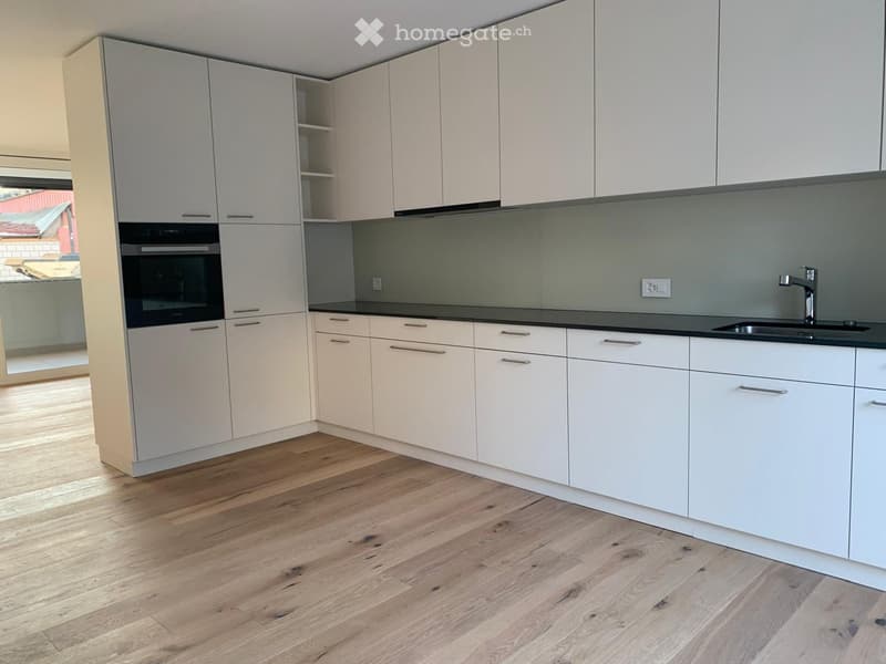 fully equipped kitchen with white cabinets, wooden floor, black countertops, stainless steel sink, dishwasher, and an oven