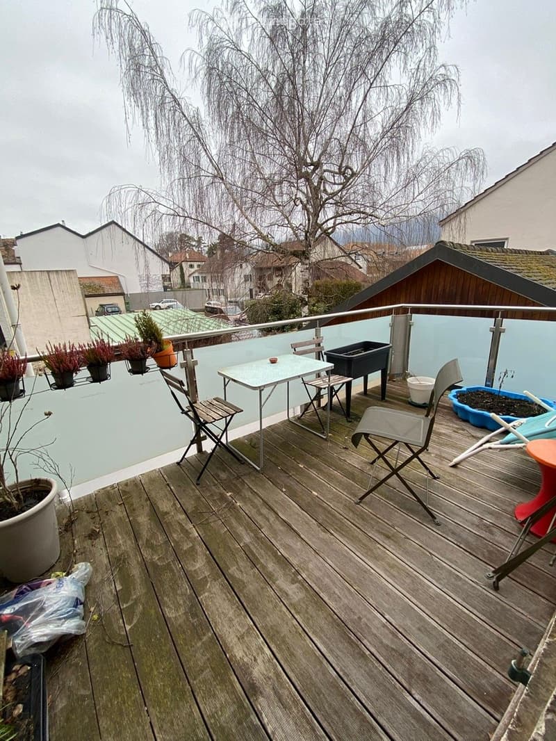 A wooden deck with chairs, a table, potted plants, and a railing