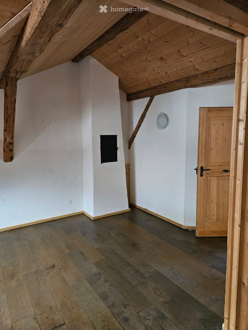 Room with wooden beams ceiling, wooden floor, white walls, wooden door, chimney