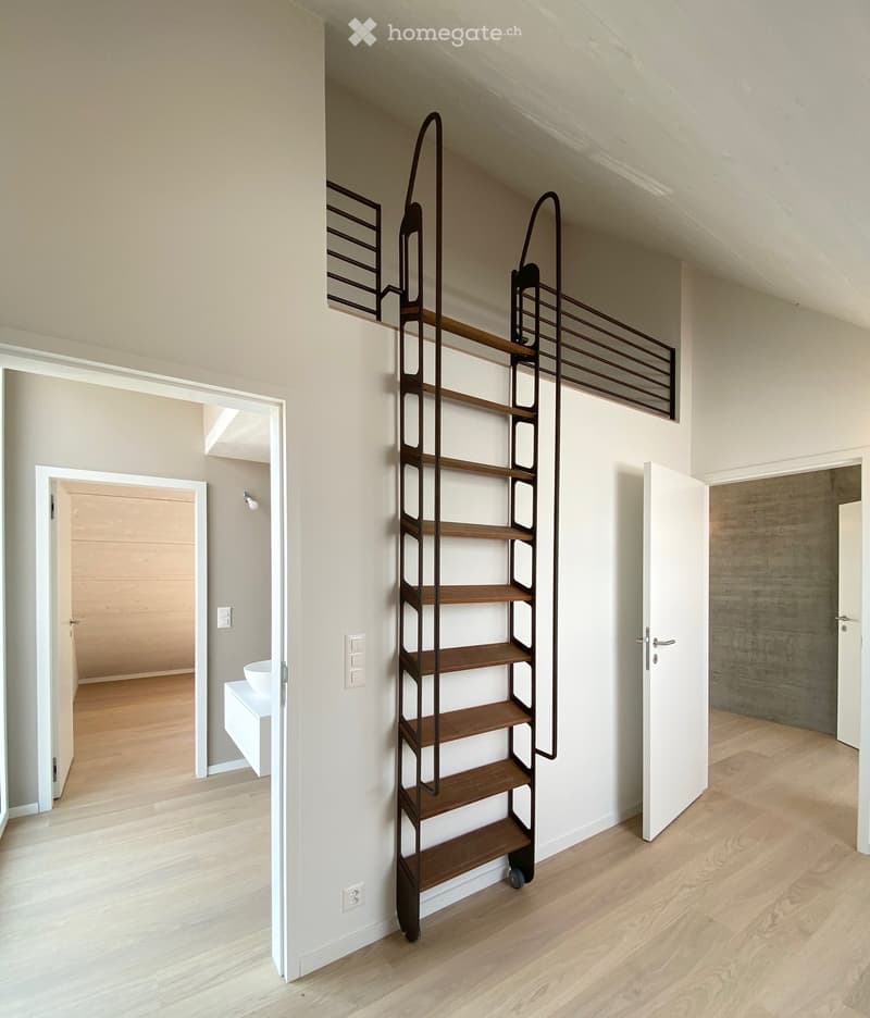 Modern hallway with light wooden flooring, white walls, and a tall, narrow shelving unit with wooden shelves and metal frame. Open doors lead to adjacent rooms, one with a visible white sink and another with a concrete wall.