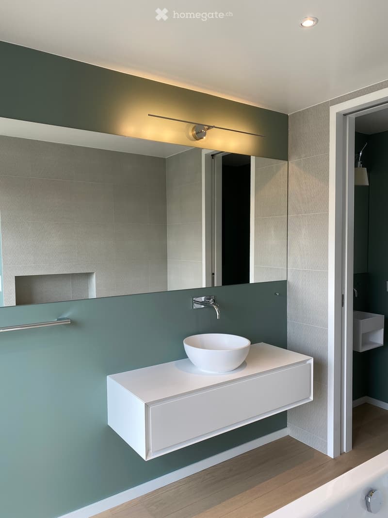 Bathroom with white sink, green wall, mirror, bathtub, wooden floor