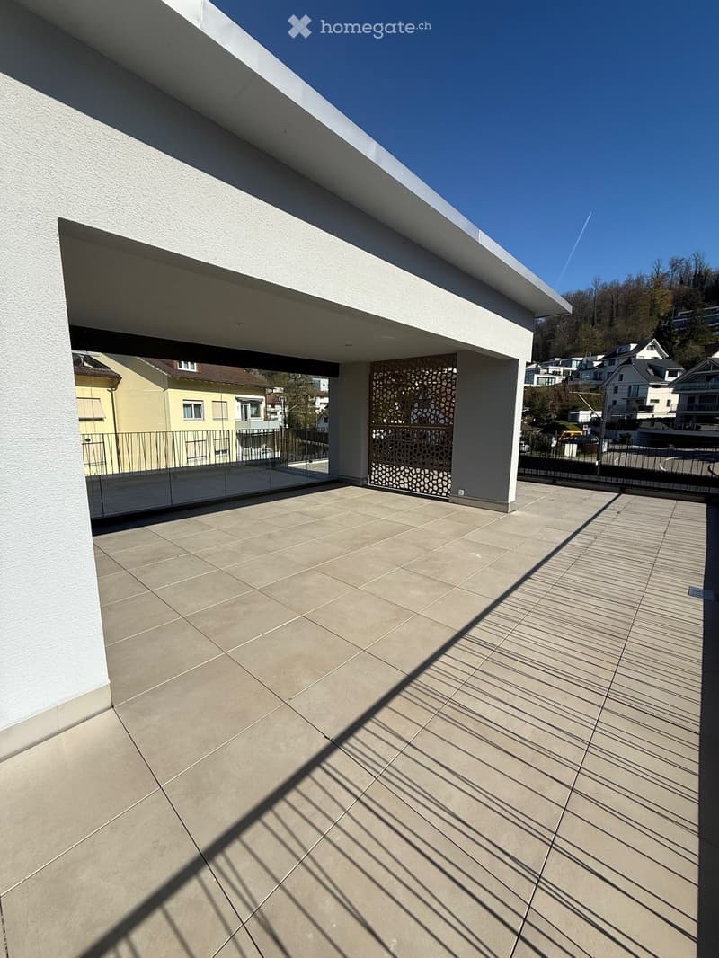 modern building with a large terrace, tiled floor, glass railings, and a view of the surrounding area