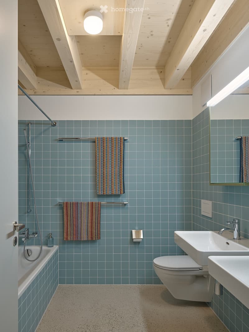 Bathroom with blue tiles, modern design, white sink, white toilet, bathtub, two towels, two towel racks, wooden ceiling