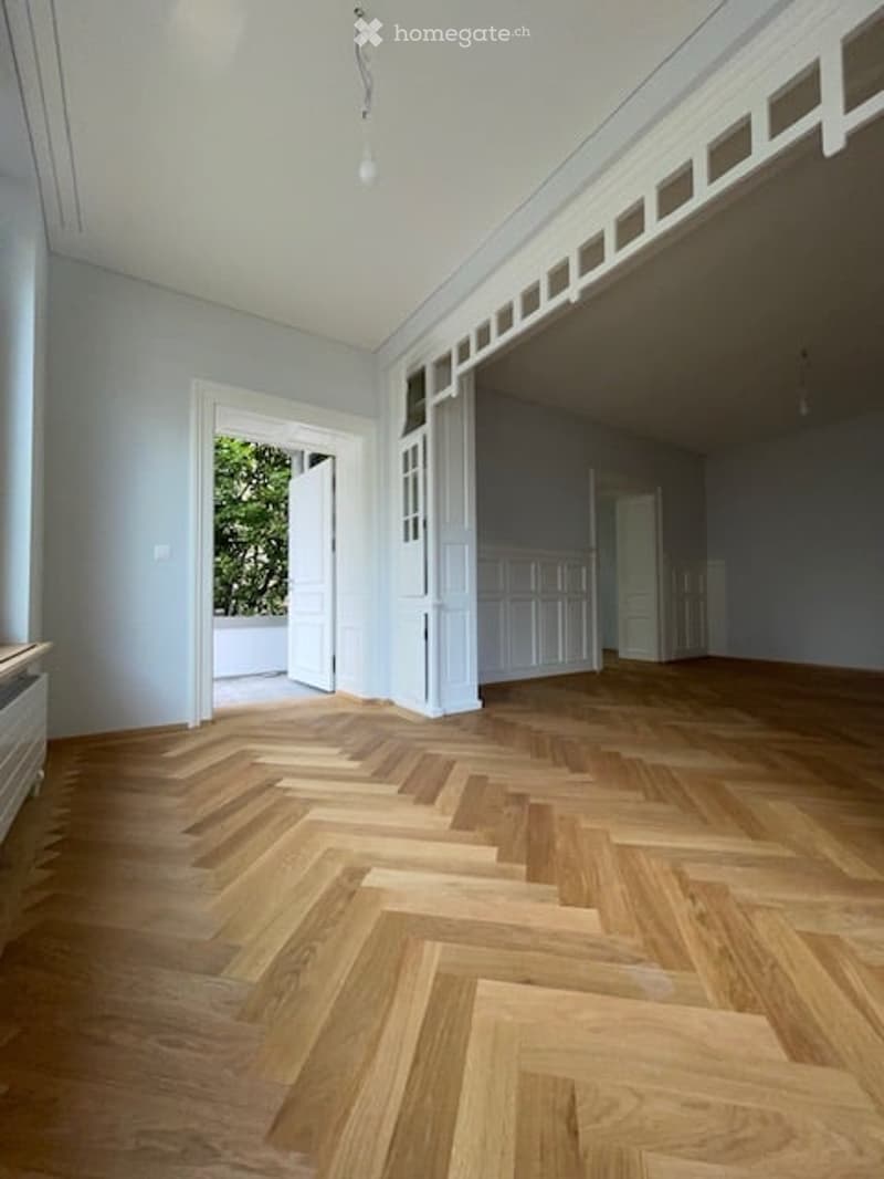 Empty room with wooden parquet flooring, white walls, white doors, and a ceiling with white trim and a hanging light fixture.
