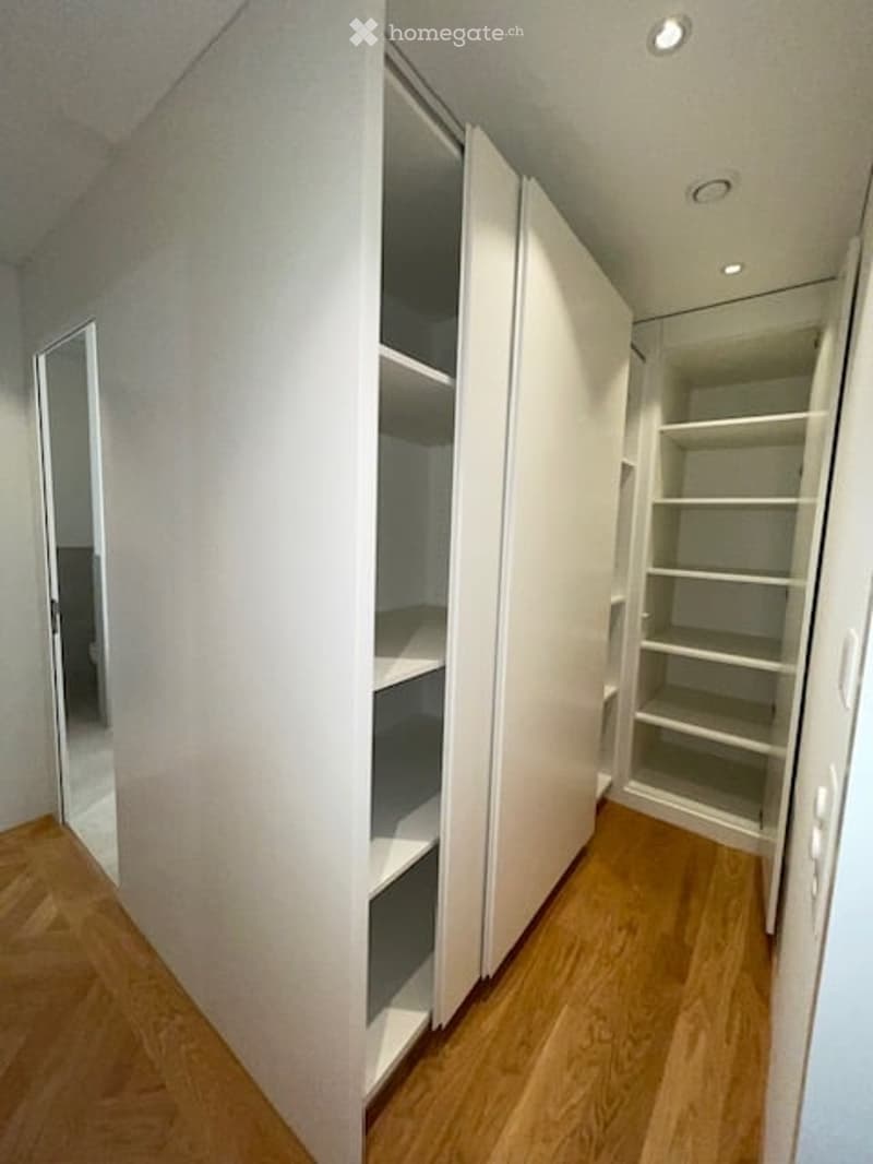 A room with a white wardrobe, wooden floor, and white walls