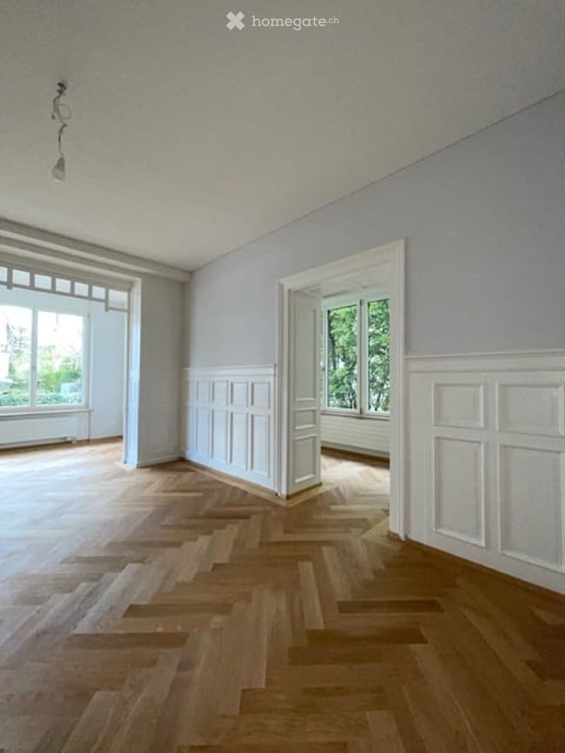 Empty room with wooden parquet floor, white walls, large windows, and a ceiling lamp