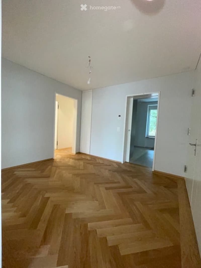 Empty room with wooden parquet flooring, white walls, and two doors leading to other rooms.