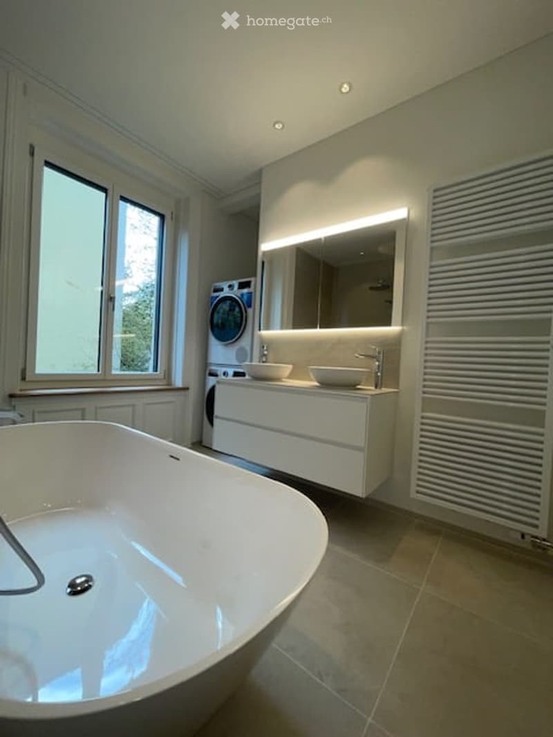 modern bathroom with bathtub, double sink, mirror, washing machine, and window