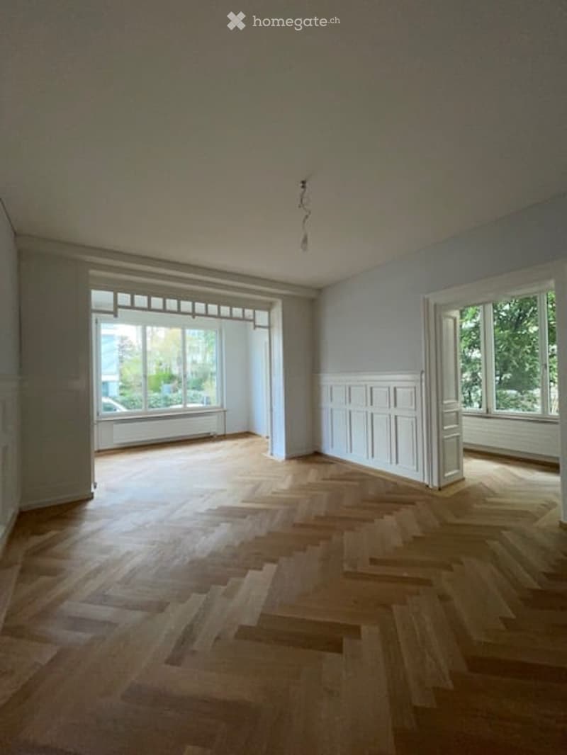 Empty room with wooden parquet flooring, white walls, large windows, and a white ceiling.