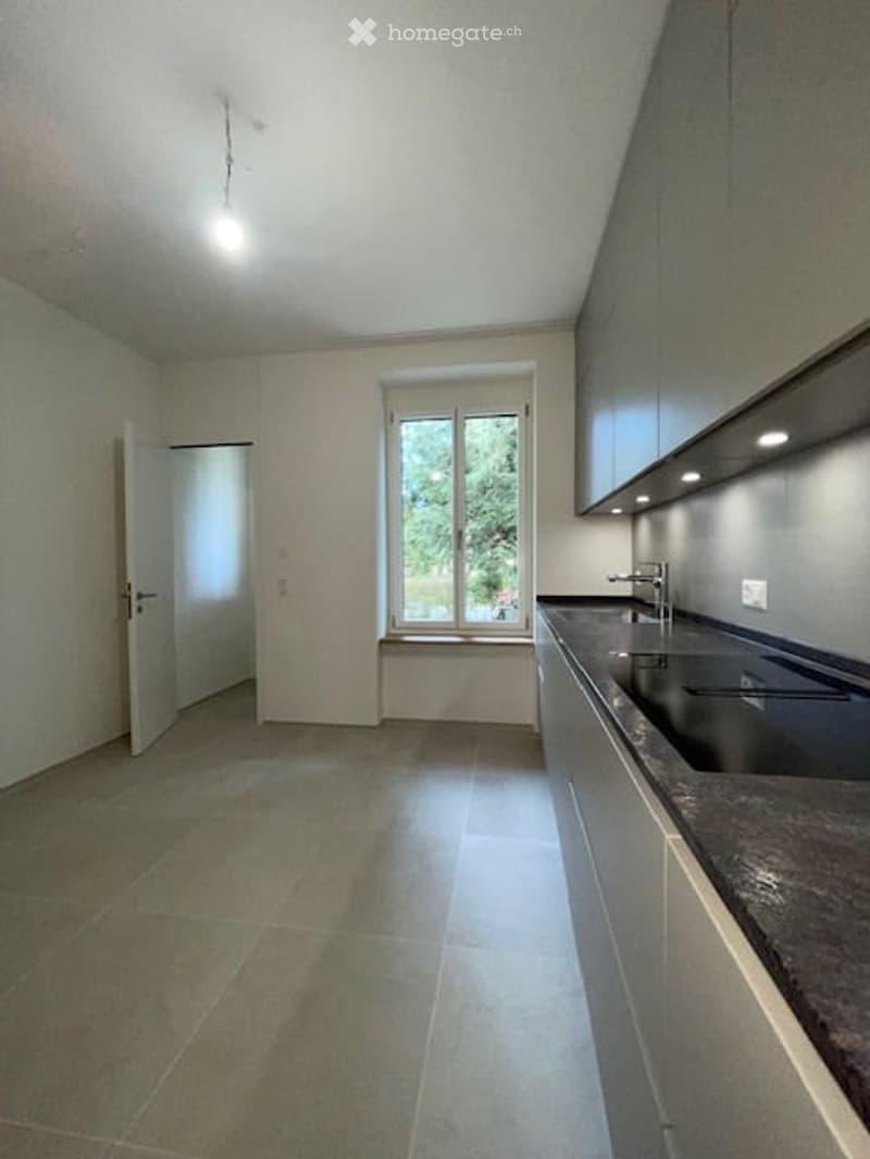 Empty kitchen with white walls, tiled floor, double sink, window, and a door