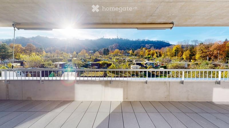 A balcony with white tiled flooring and a white railing, offering a view of a garden and mountainous area