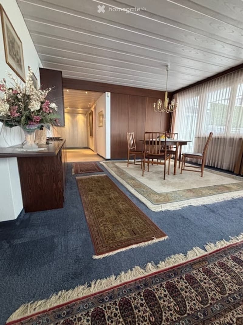 room with carpet, wooden desk, dining table with chairs, chandelier, flower vase, wooden panels