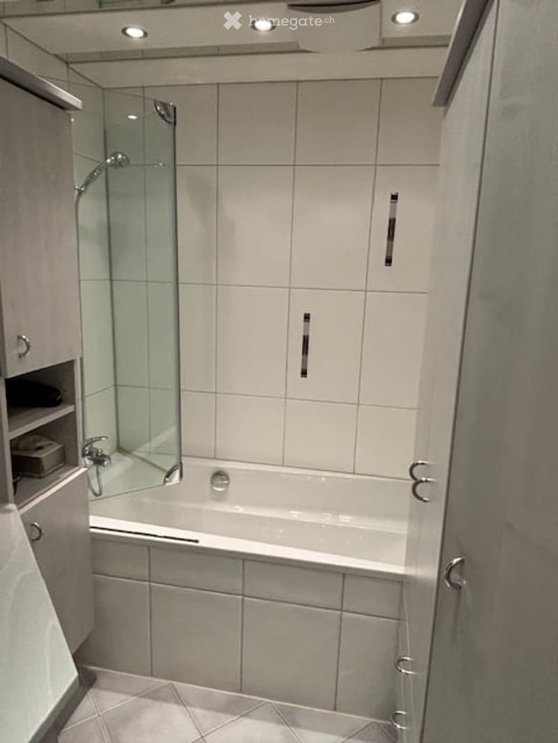 white tiled bathroom, bathtub, shower, glass door, storage shelves, and white tiles