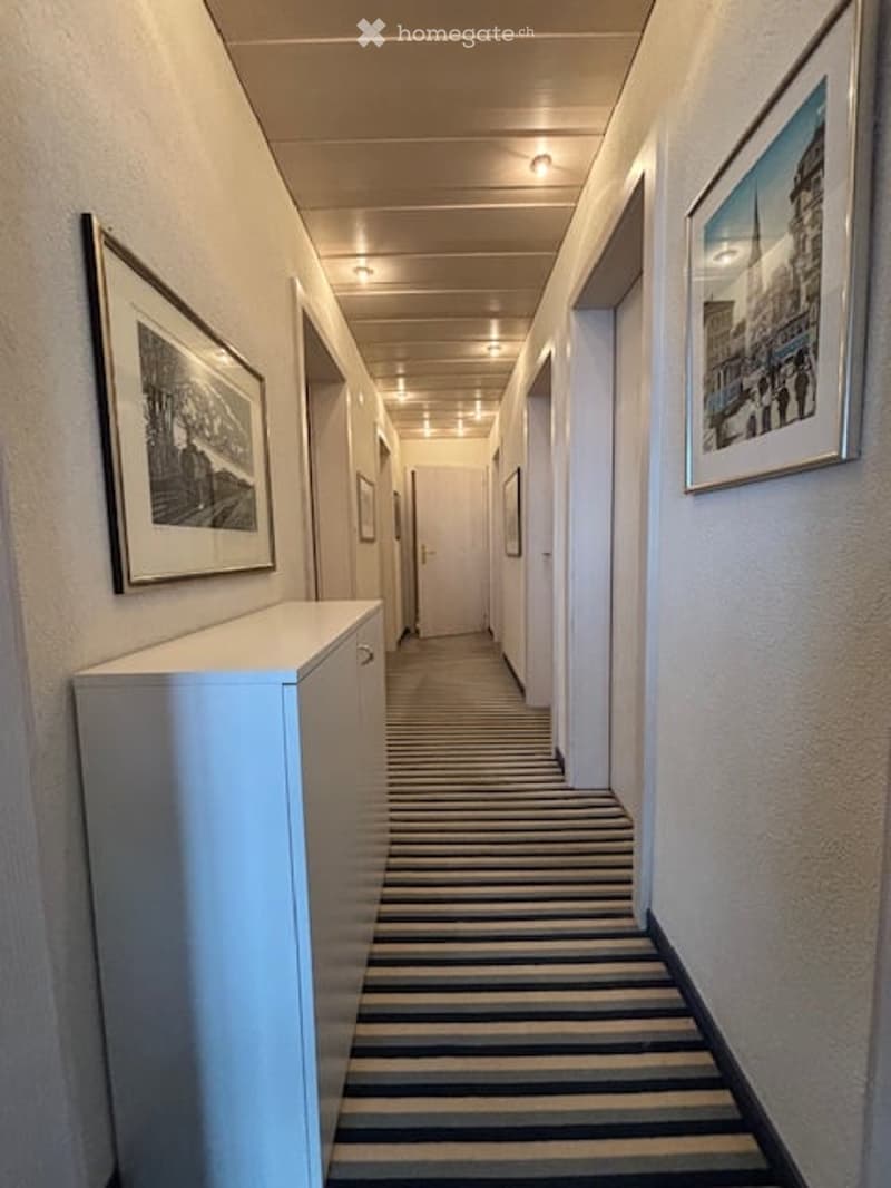 Striped floor, white walls, two framed pictures on the wall, white cabinet, two doors