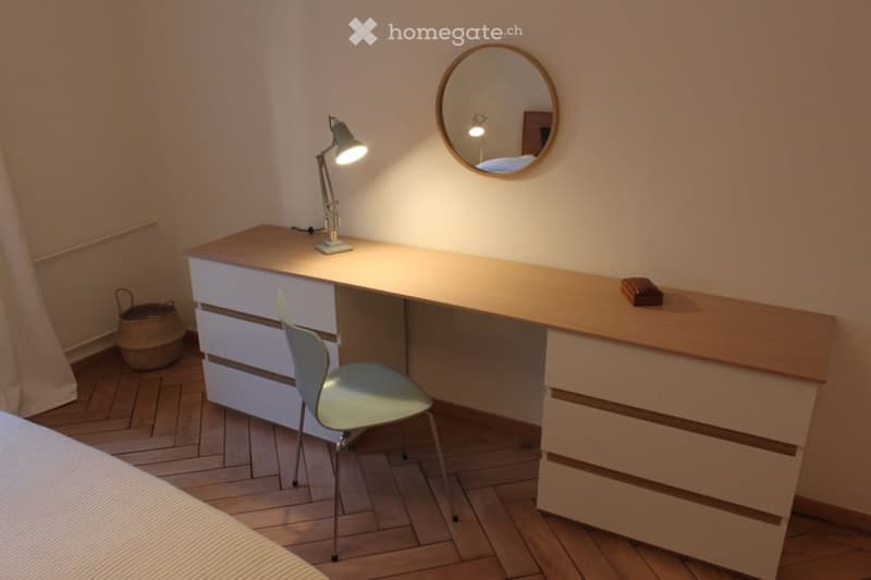 Desk with drawers, a lamp, a round mirror, a chair, a basket on the floor