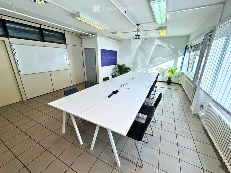 A meeting room with white tiled floor, long table, chairs, whiteboard, a window with blinds, radiator, a plant near the window, and an office door.